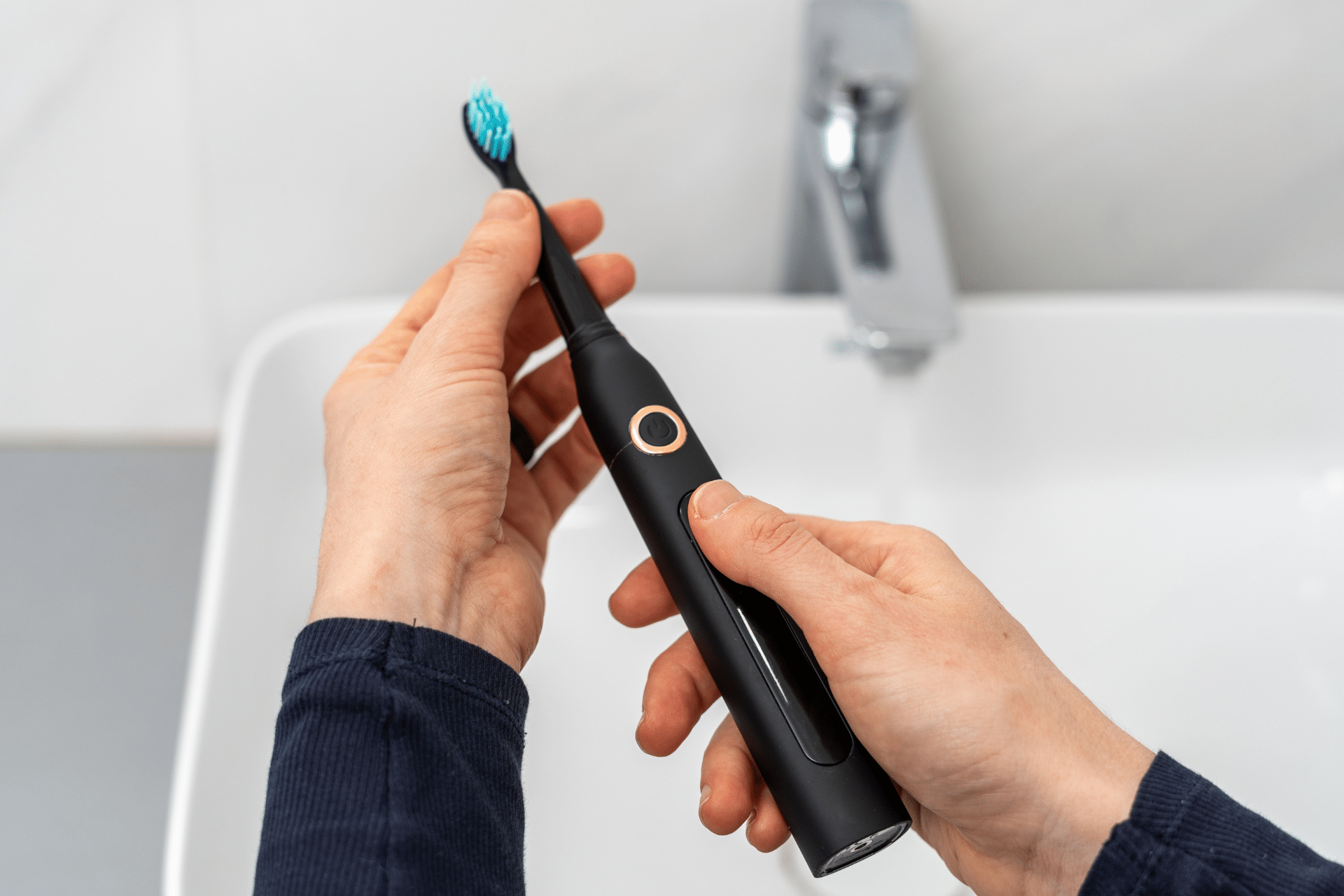 A person holds a black electric toothbrush over a bathroom sink, illustrating the problem of bleeding gums.